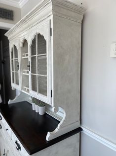 an old china cabinet is painted white and has black countertop, with a potted plant on top