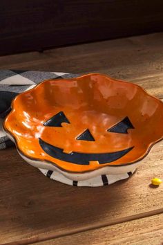 an orange and black pumpkin shaped bowl sitting on top of a wooden table next to candy