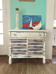 an old dresser is painted white with blue and red stripes on the bottom, along with a sailboat painting