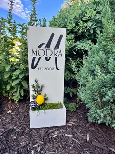 a sign that says modra next to some bushes and trees in front of it