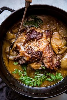 a pot filled with meat and potatoes covered in gravy, garnished with parsley