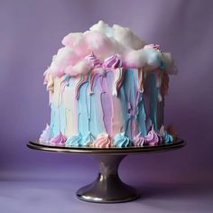 a cake with pastel icing and clouds on it sitting on a metal platter