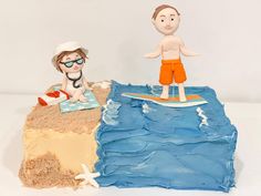 there is a cake made to look like two people on the beach, one standing on a surfboard