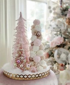 a pink and white christmas tree is on top of a gold tray in front of a decorated christmas tree