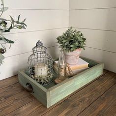 a wooden tray with some plants and candles on it next to a potted plant