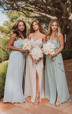 three bridesmaids pose for a photo in front of a tree with their bouquets