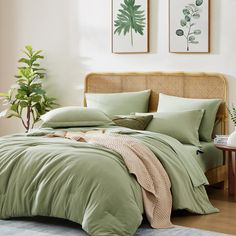 a bed with green comforters and pillows in a white room next to a potted plant