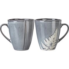 two coffee mugs sitting side by side on top of each other, one with a leaf design