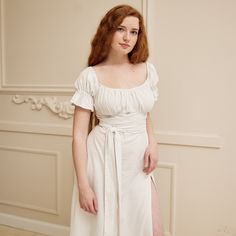 a woman with red hair wearing a white dress and standing in front of a wall