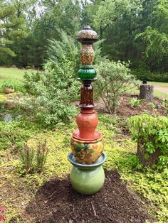 a tall tower made out of pots in the middle of a garden with trees and bushes behind it