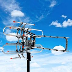 a television antenna on top of a pole with clouds in the back ground and blue sky behind it