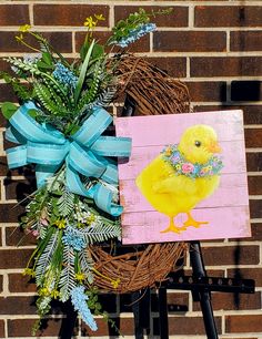 a painting of a yellow duck on a easel next to a wreath with blue ribbon