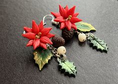 two red poinsettias are hanging from earrings on a black surface with pine cones and acorns