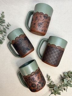 four coffee mugs sitting on top of a table next to some leaves and flowers