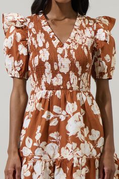 The dress for your next brunch date is our lovely Surrey Floral Leones Smocked Mini Dress. A white floral print sits on brown background with cotton fabric. Features a ruffle trim V neckline and fully smocked bodice framed by short puff sleeves. It tops a flared ruffle tier mini skirt. Wear it white loafers and gold accessories. - Breathable- Smocked bodice- Ruffle details- Pockets- Color: Rust CreamSize + Fit - Model is 5'9" and wearing size XS- Measurements taken from size S - Chest: 14 1/2"- Brown Smocked Back Dress For Brunch, Brown Cotton Floral Print Dress, Brown Smocked Bodice Dress For Brunch, Brown Dresses With Smocked Back For Brunch, Brown Dress With Smocked Back For Brunch, Brown Floral Print Puff Sleeve Dress, Brown Puff Sleeve Floral Print Dresses, Smocked Mini Dress, White Loafers