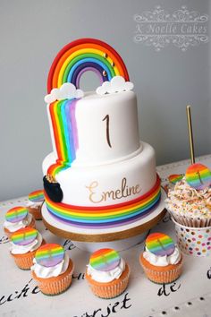 a rainbow themed cake and cupcakes on a table