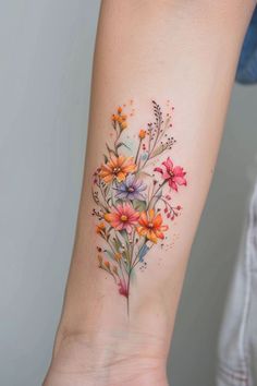 a woman's arm with flowers on it and watercolors in the background