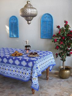 a blue table cloth on top of a wooden table next to potted plants and vases