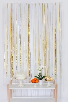 a white table topped with a cake next to a wall covered in streamers and confetti