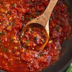 a wooden spoon in a pot filled with tomato sauce