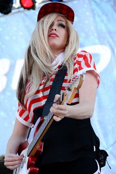 a woman with long blonde hair playing an electric guitar at a music festival in front of a large screen