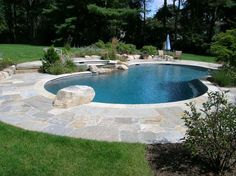 a swimming pool surrounded by stone steps and green lawn area with trees in the background