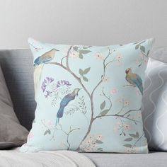 a blue pillow with birds and flowers on it sitting on a couch next to pillows