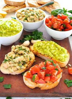 three bowls of guacamole, tomatoes and bread on a wooden cutting board