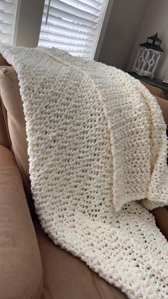 a white crocheted blanket sitting on top of a couch next to a window