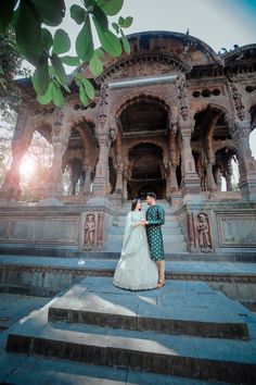 a bride and groom standing on steps in front of an ornate building with sun shining through the trees