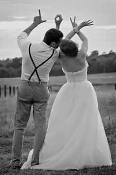 a man and woman standing in the grass with their arms raised up to each other