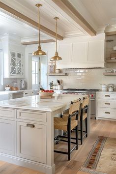 a large kitchen with white cabinets and wooden flooring, two pendant lights hanging over the island