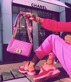 a woman sitting on the ground with pink shoes and a chanel bag in front of her