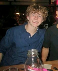 two young men sitting at a table with drinks in front of them and one is smiling for the camera