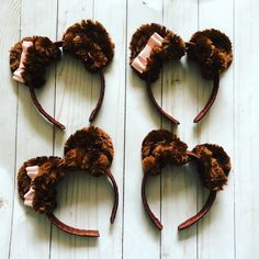 four brown mouse ears with bows on top of white wooden planked floor and one has pink ribbon in the middle