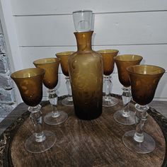 a brown vase sitting on top of a wooden table next to glasses and a bottle