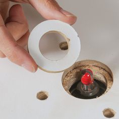 a hand is holding a piece of paper near a hole in the wall with a red light on it