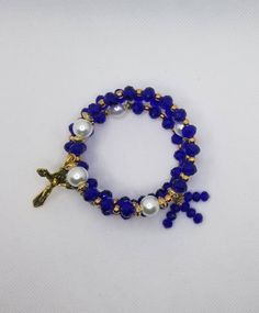 This 3 to 4 loop gold-toned metal memory wire wrap bracelet is a full five-decade rosary, complete with a crucifix. It's made on memory wire, which is a type of spring steel that can spring back when stretched out. It has 8mm faceted Czech rondelle beads in cobalt blue for the decade beads and 10mm white glass pearls for the Father beads. The spacer beads are 4mm rose gold beads. There are disc-shaped gold metal spacer beads as well. It features a gold-toned metal crucifix on one end and three m Adjustable Gold Hand Wrapped Rosary Bracelet, Gold Handmade Cross Rosary Bracelet, Gold Beaded Rosary Bracelet With Cross Shape, Beaded Cross Jewelry For First Communion, Cross-shaped Beaded Jewelry For First Communion, Handmade Blue Crucifix Jewelry, Adjustable Blue Rosary Bracelet With Cross, Adjustable Beaded Rosary Bracelet With Crucifix, Adjustable Blue Cross-shaped Jewelry