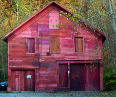 an old red barn sits in the woods