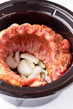 an open crock pot filled with meat and onions on top of a white table