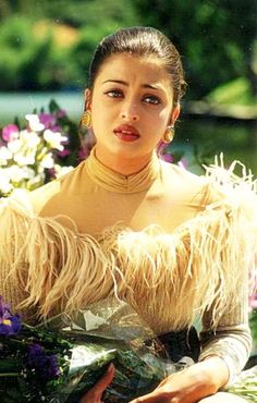 a woman sitting on the ground with flowers in front of her and looking at the camera