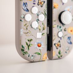 a close up of a controller with flowers and butterflies painted on the front, along with two white buttons