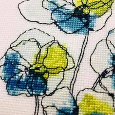 a cross stitch picture of three flowers with blue and yellow petals on white fabric,