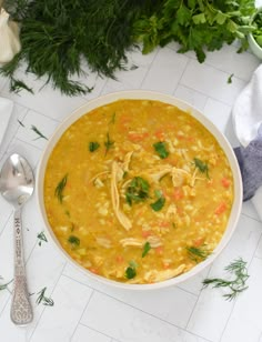 a white bowl filled with chicken and carrots next to some herbs on the table