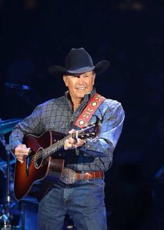 a man wearing a cowboy hat and holding a guitar in his right hand while standing on stage