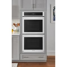 two ovens side by side in a kitchen with gray cabinets and white counter tops