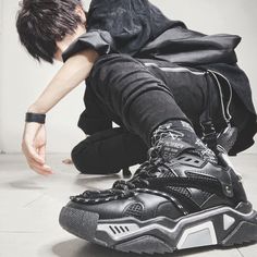 a young man sitting on the floor with his foot up to his face and wearing black sneakers