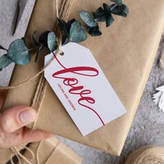 a person holding a wrapped gift with the word love on it and tied in twine