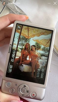 a person holding up a cell phone with two women on the screen and an umbrella in the background