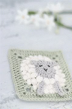 a crocheted square with a white and gray sheep on it next to flowers